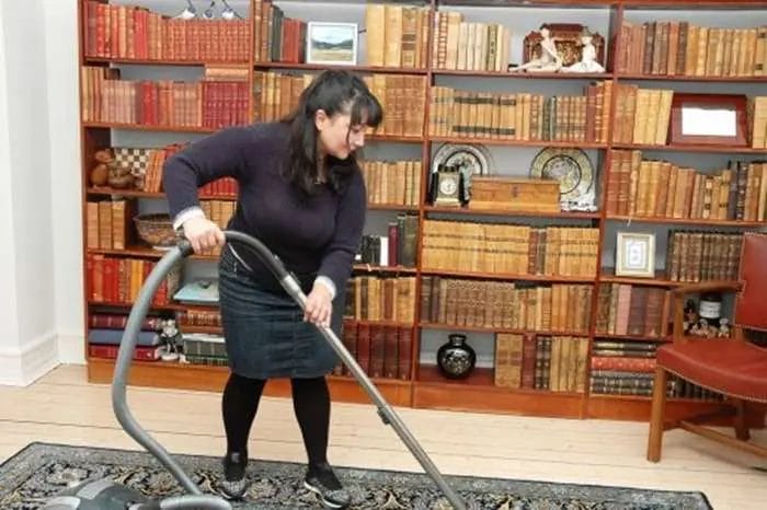Kvinde støvsuger tæppe foran bogreol.